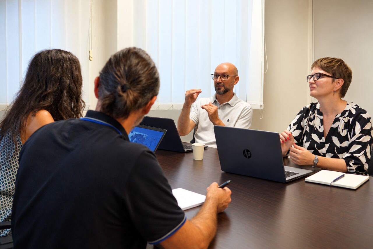 Roncucci&Partners team 4 consultants talking around a table. In front of them, laptops