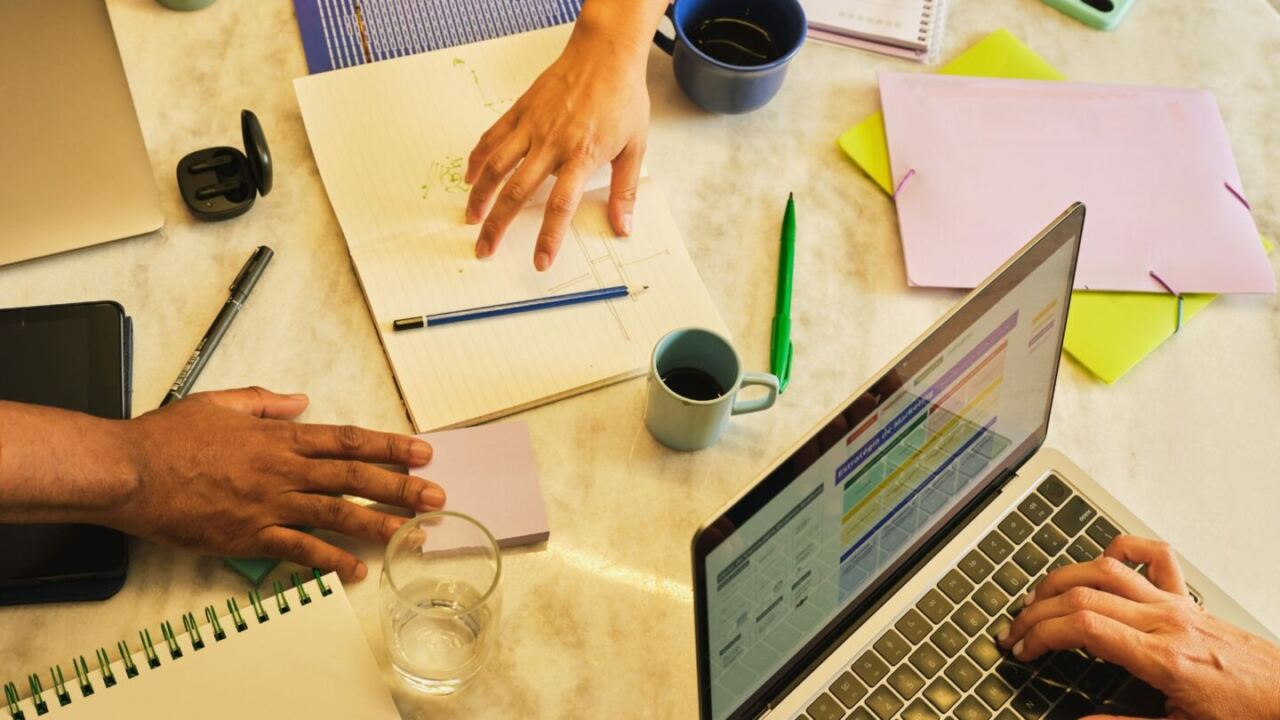 mani di persone che indicano cose su documenti, con intorno carte, penne, e computer